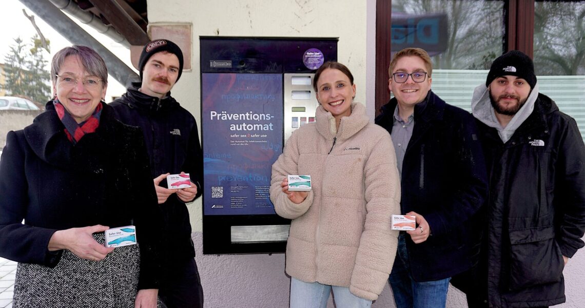 Vertreter von Diakonie und AIDS-Hilfe stehen vor dem neuen Präventionsautomaten, sie halten Päckchen mit Safer Use-Materialien in der Hand.